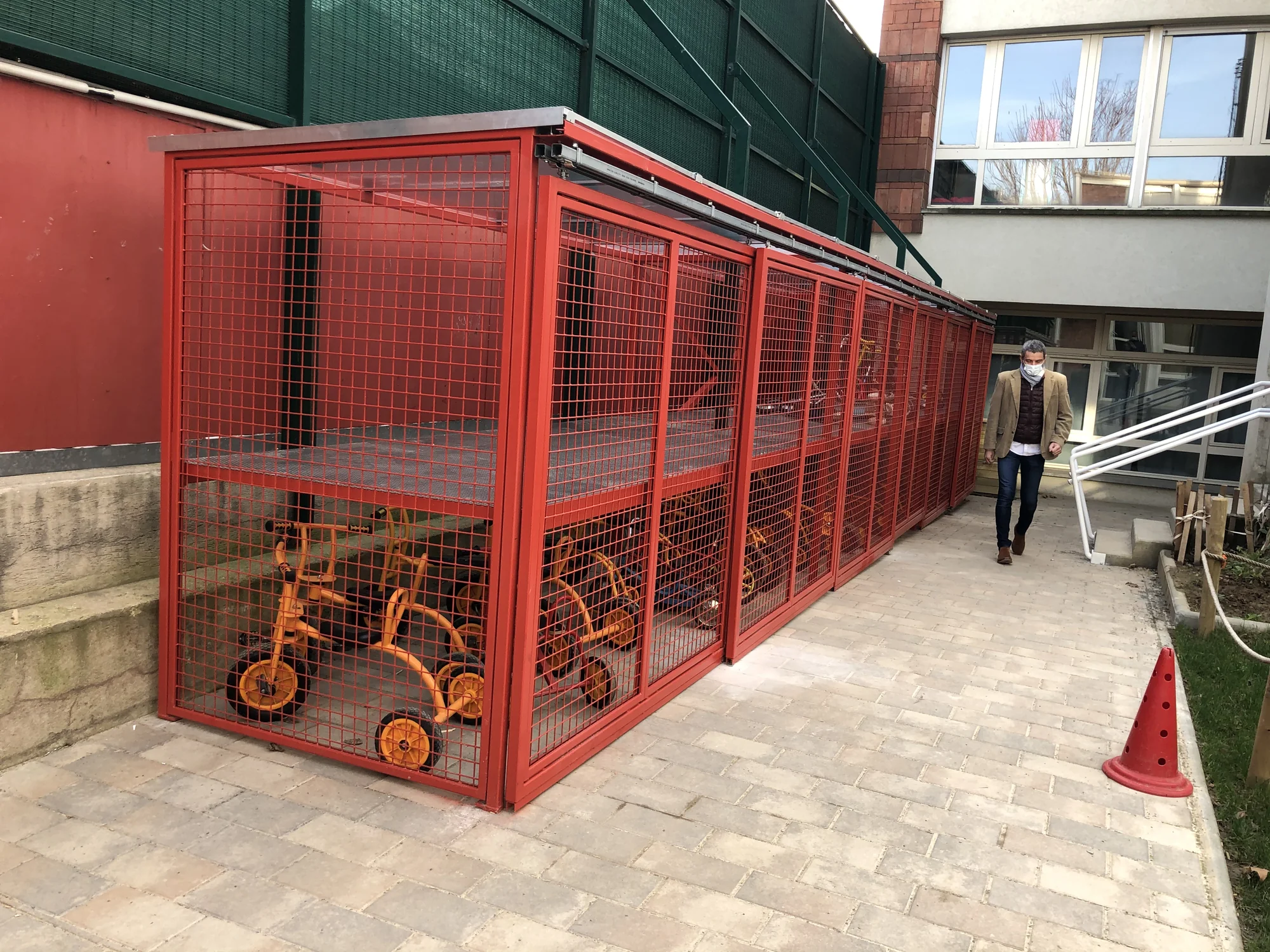 Vue d’ensemble du local vélo grillagé dans la cour d’une école primaire